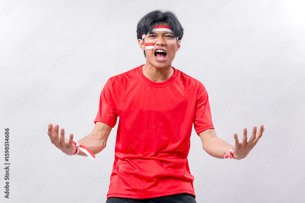 Naklejka premium Young Indonesian man with face paint, red shirt, and expressive pose shouting with passion. Celebrating Independence Day with full spirit and national pride on a special occasion.
