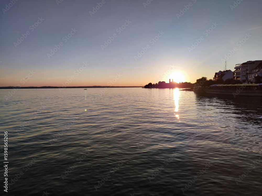 Naklejka premium Peaceful sunrise over a wide lake, soft reflections shimmering on the water.