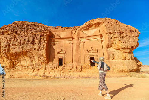 Tourist pointing at ancient Nabataean rock-cut tombs of Jabal Al-Ahmar in Hegra archaeological site, Al-Ula, Madinah, Saudi Arabia, a UNESCO World Heritage site with stunning sandstone formations