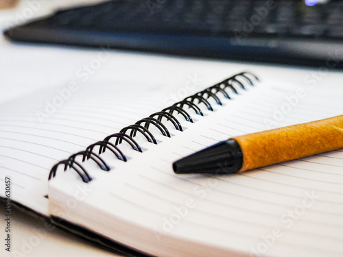 фотографія Brown ballpoint pen resting on a white spiral notebook, with a keyboard in the background