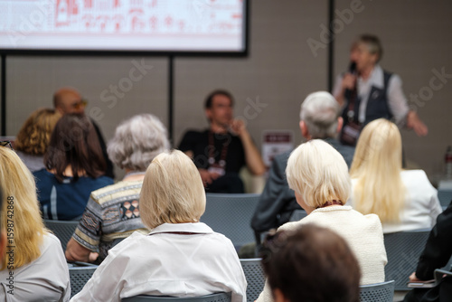 Attentive audience members focus on a speaker presenting at a professional conference or seminar.