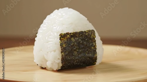 Close-up of a single onigiri rice ball with nori seaweed on a wooden plate
