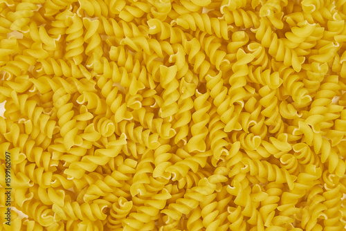 Full image of raw fusilli pasta, with a patterned background and copy space