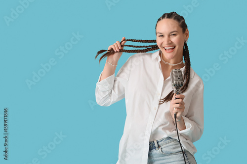 Young woman with dreadlocks and microphone singing on blue background