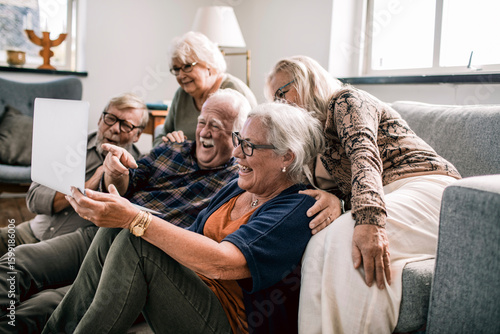 Group of senior friends laughing together while watching something on laptop