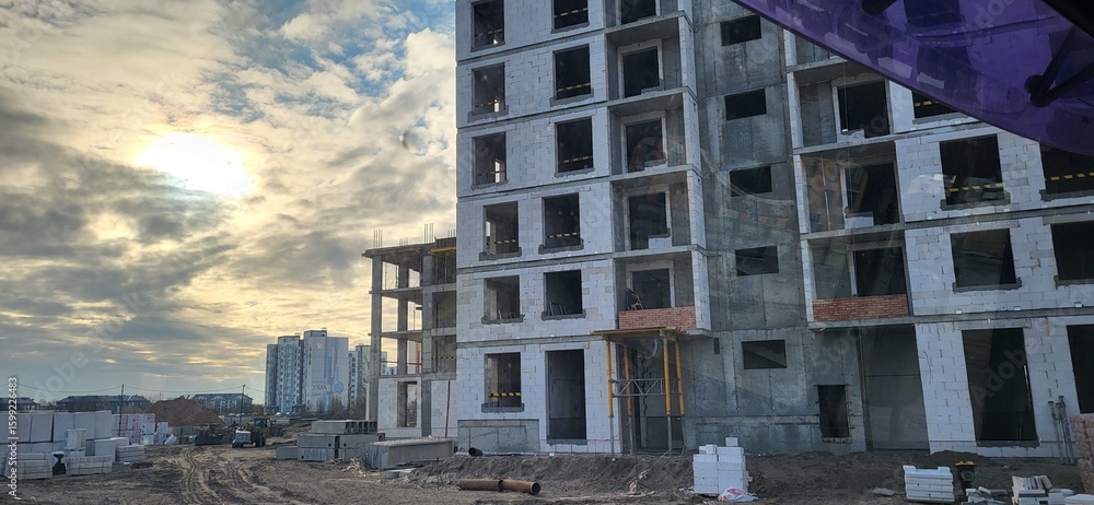 Fototapeta premium Construction of modern residential buildings at sunset with workers active on site