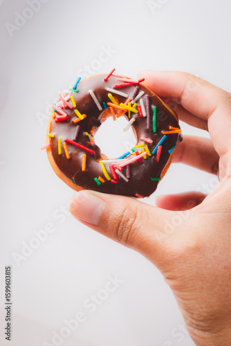 Hand Holding Chocolate Sprinkle Donut Against Neutral Background