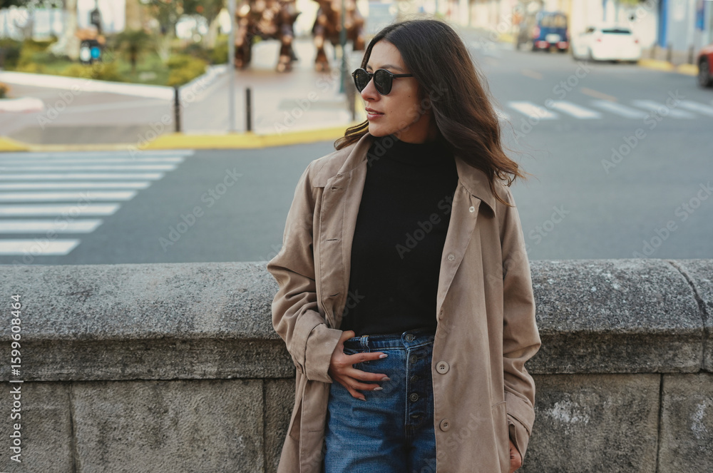 Obraz premium Stylish woman wearing trench coat and sunglasses posing in urban setting