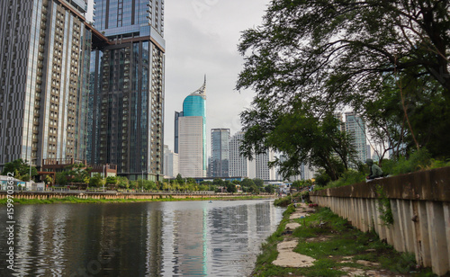 view of a public park with a lake in Jakarta in the morning with a background of modern buildings on the lake side