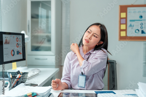 Fotografie Young professional woman massaging her shoulder in a modern office, experiencing
