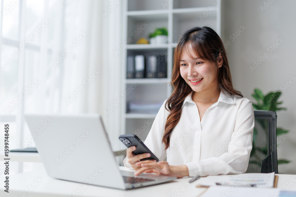 Smiling businesswoman using laptop and smartphone while working in modern office, managing her business and connecting with clients and colleagues efficiently Smiling businesswoman using laptop and smartphone while working in modern office, managing her business and connecting with clients and colleagues efficiently