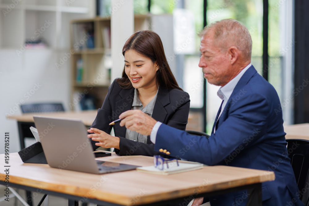 Obraz premium Mature manager mentor talking to Asian female coworker, showing online project results at Business partners in meeting. Two happy diverse professional executives team working on laptop in office 