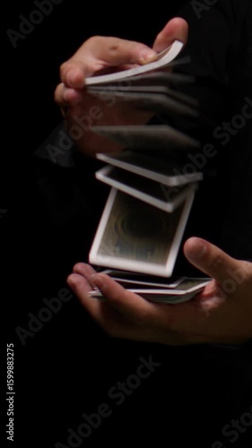 A skilled cardist performs a mesmerizing flourish, displaying agile control as cards cascade smoothly between their hands, creating an elegant arc against a dark background.
