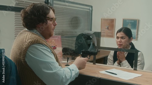 Unprofessional male robber demanding money from cashier at clients window pointing gun at woman then taking wads of cash and leaving bank with pregnant female partner