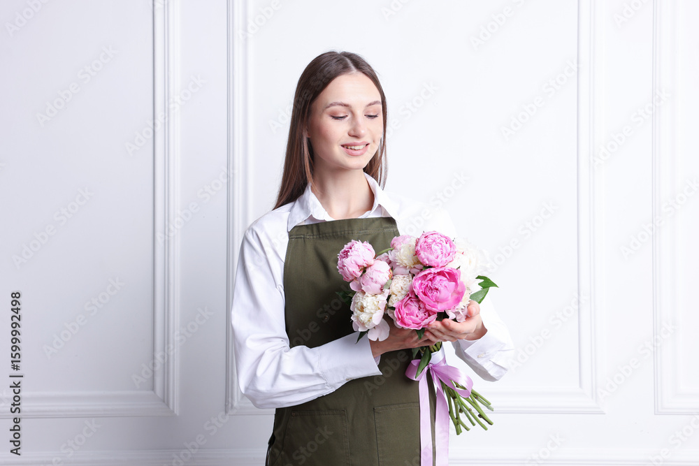 Florist with beautiful bouquet of peonies near white wall indoors Florist with beautiful bouquet of peonies near white wall indoors