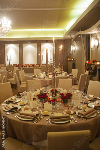Stylish banquet hall featuring round tables adorned with formal table settings, floral arrangements, and elegant lighting, creating a luxurious atmosphere for celebrations or events.