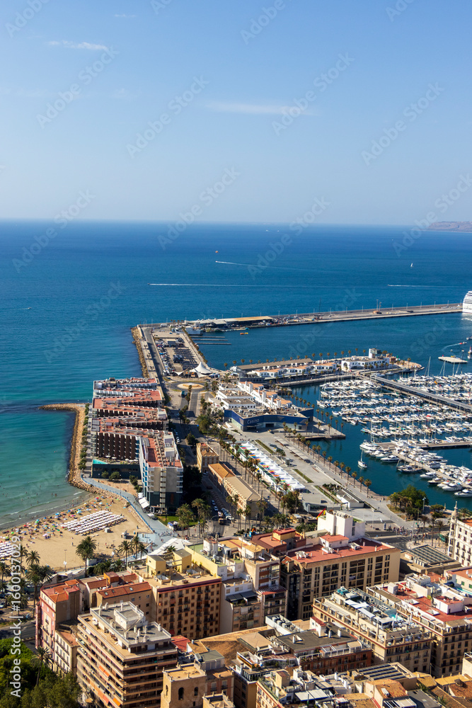 Naklejka premium A panoramic view of Alicante's coastline featuring picturesque beaches, bustling marina, and vibrant urban architecture under clear blue skies. Ideal for travel and lifestyle applications.