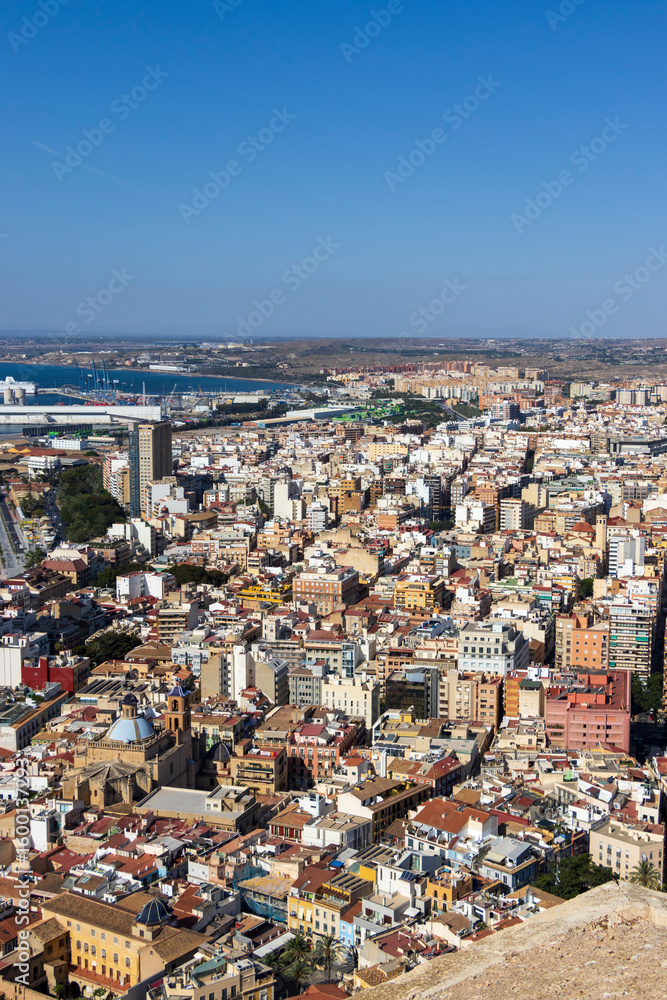 Obraz premium Aerial view of Alicante showcasing vibrant urban architecture, with a blend of traditional and modern buildings against a clear blue sky, highlighting the dynamic city life.