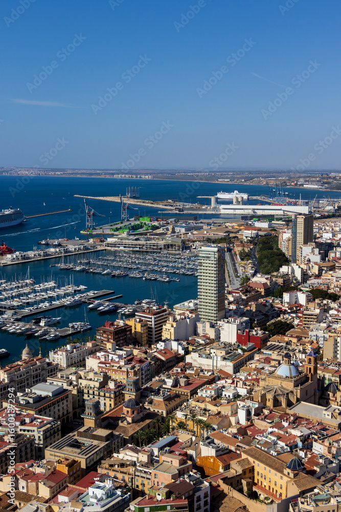 Fototapeta premium A panoramic view of Alicante, showcasing the bustling harbor, vibrant cityscape, and clear blue sky, illustrating maritime activities and urban life.