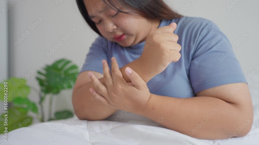 Asian plus-size woman sit on bed in morning, holding her aching hand. Asian plus-size woman sit on bed in morning, holding her aching hand.