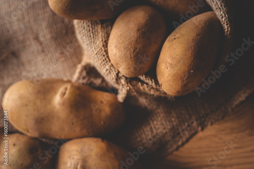 Billede på lærred Fresh raw potatoes in a rustic burlap sack on a wooden surface
