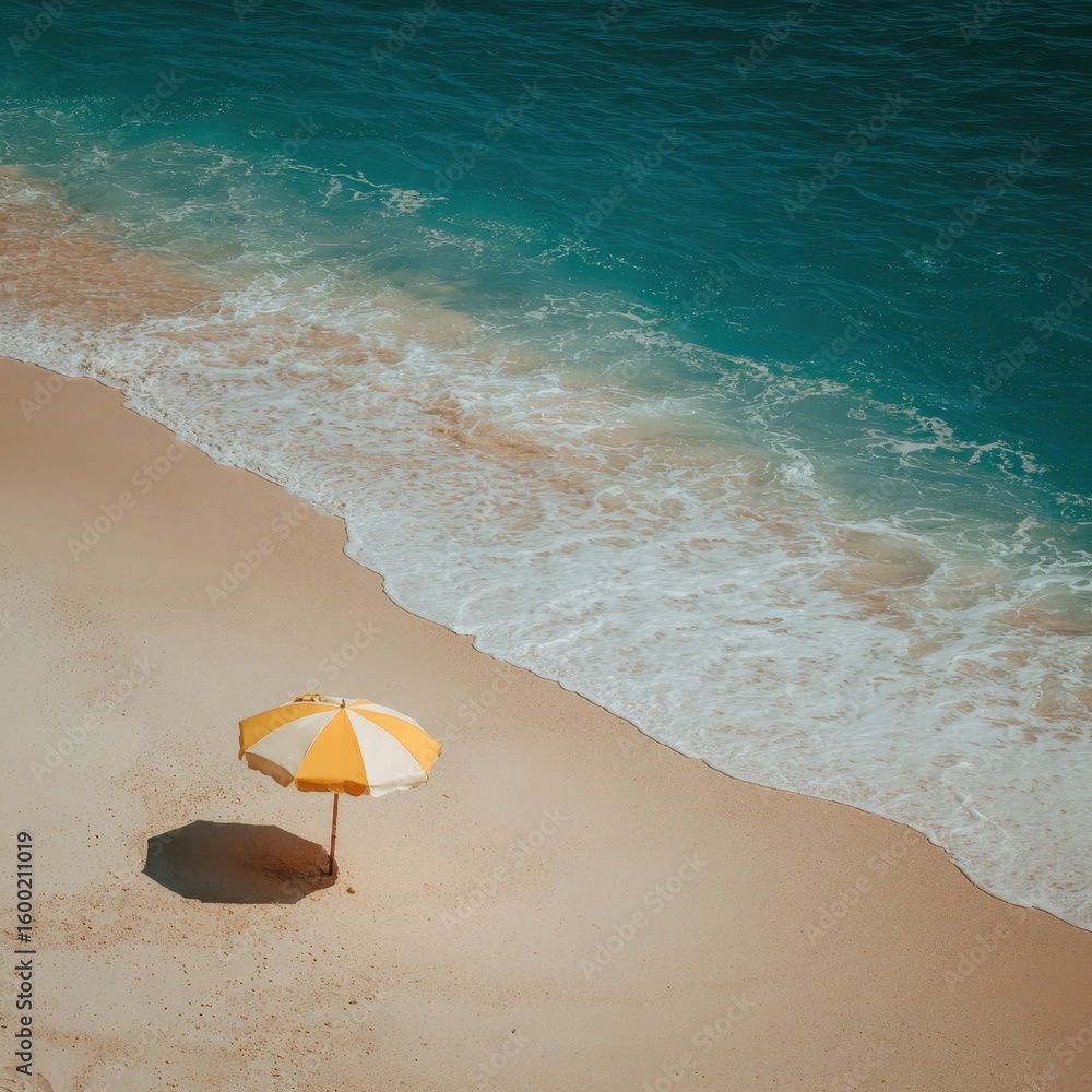 A lone yellow striped umbrella on a sandy beach meets the turquoise ocean A lone yellow striped umbrella on a sandy beach meets the turquoise ocean