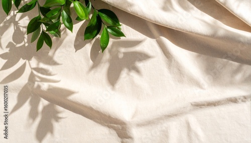 Minimalist abstract background of a soft green leaf shadow on a textured, neutral beige linen fabric.


