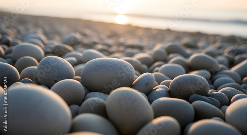 A close up view of smooth stones on a beach with the sun setting in the distance over the ocean