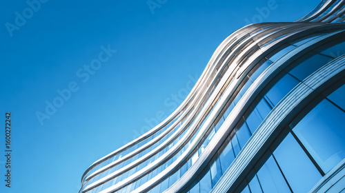 A close-up of the curved glass facade on an office building, showcasing its sleek design against a clear blue sky.