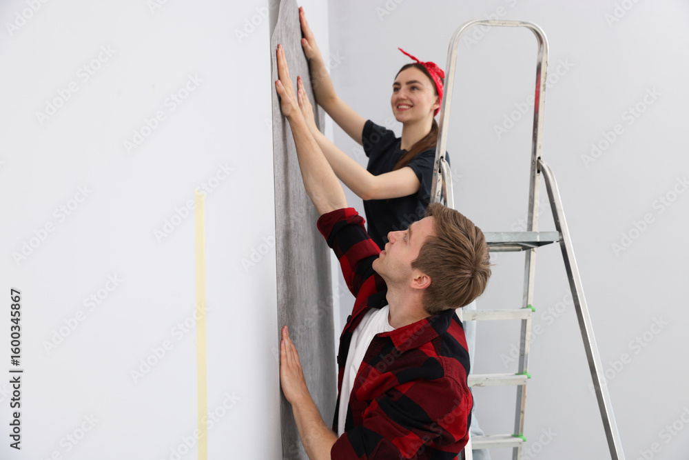 Obraz premium Happy couple putting wallpaper on wall in room
