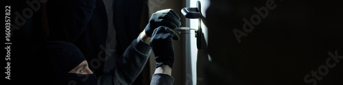 Fototapete Burglar wearing black mask and gloves picking door lock with metal tool in dark