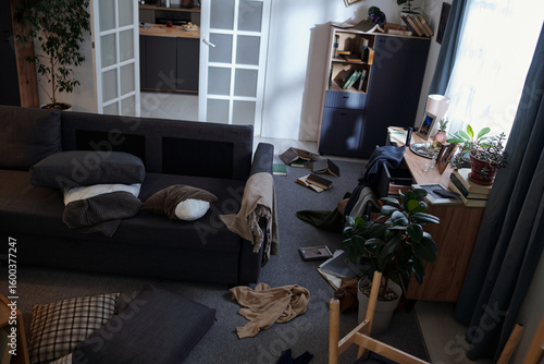 Принти на полотні Living room scene showing scattered books, pillows, and clothing on floor near s