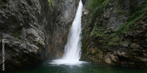 Tall waterfall cascades in narrow canyon, creating dramatic scene