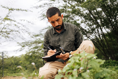 Φωτογραφία Male biologist writing in notebook while observing plants in natural environment