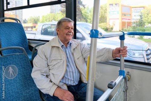A portrait of an elderly man in casual clothes, sitting on a public bus and looking out the window.
