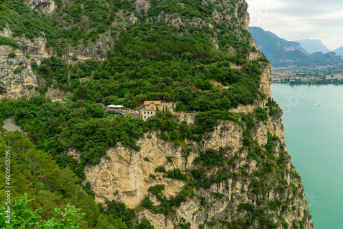 Cliffside road and buildings surrounded by greenery above a lake.