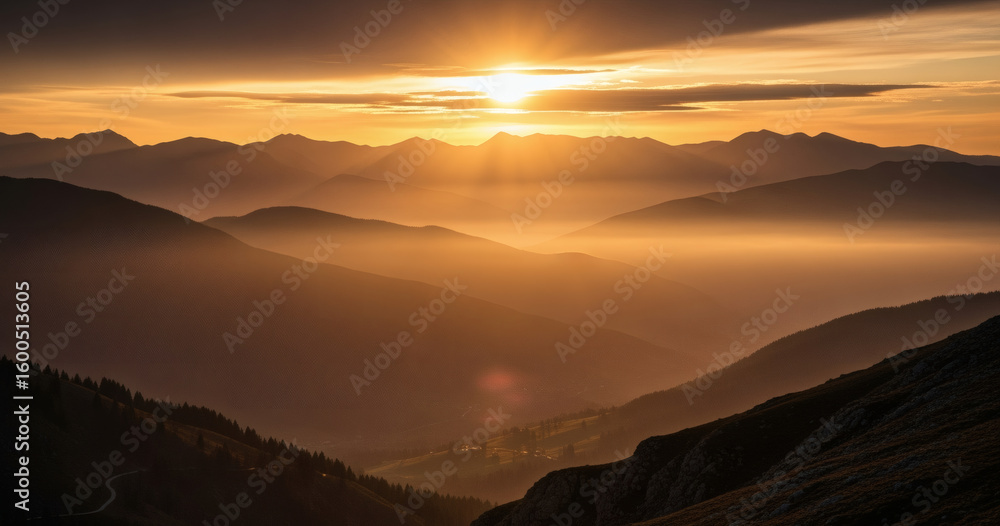 Obraz premium Majestic sunset over a hazy mountain range, golden light illuminating distant peaks.