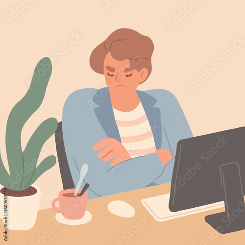 Young man sitting at desk with arms crossed and frowning at computer  