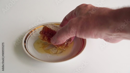 A man's hand takes a piece of honeycomb from a saucer to eat it.