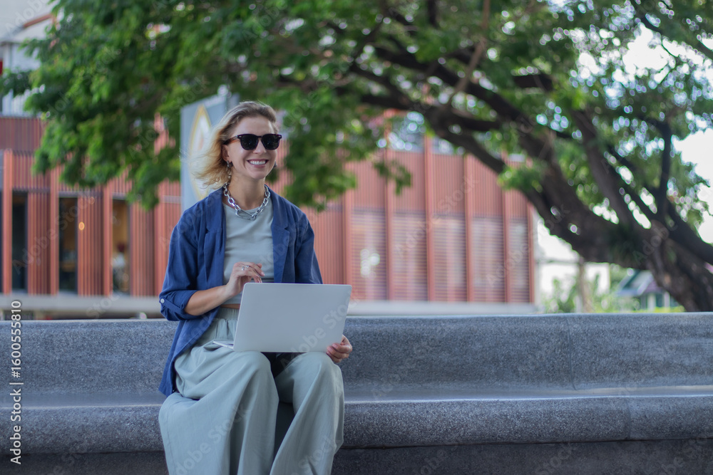 Obraz premium Smiling mature woman in suit with coffee and laptop on balcony. Confident and elegant entrepreneur contemplating success, happiness and desires.