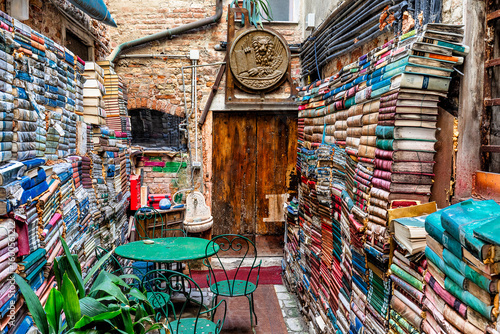 View of vibrant stacks of books create colorful walls around a cozy outdoor seating area in a hidden corner, Venice, Veneto, Italy.