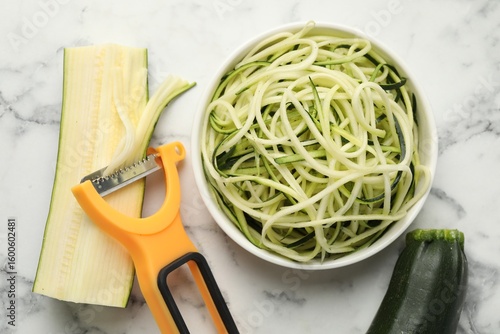 Photos Raw zucchini noodles, peeler and fresh vegetables on white marble table, flat lay