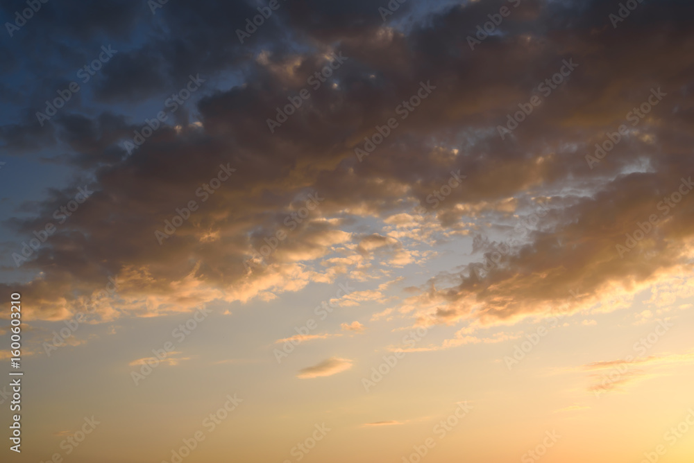 Fototapeta premium A tranquil evening sky featuring soft clouds illuminated by the warm hues of a setting sun.