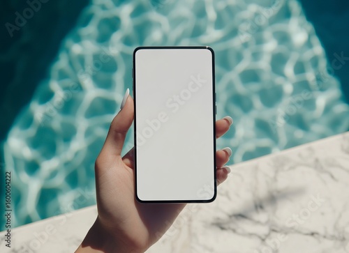 A woman's hand holding a blank-screen mobile phone with a notebook on a white marble table, viewed from a high angle. This is a stock photo mockup template with blank space for text or design. High re