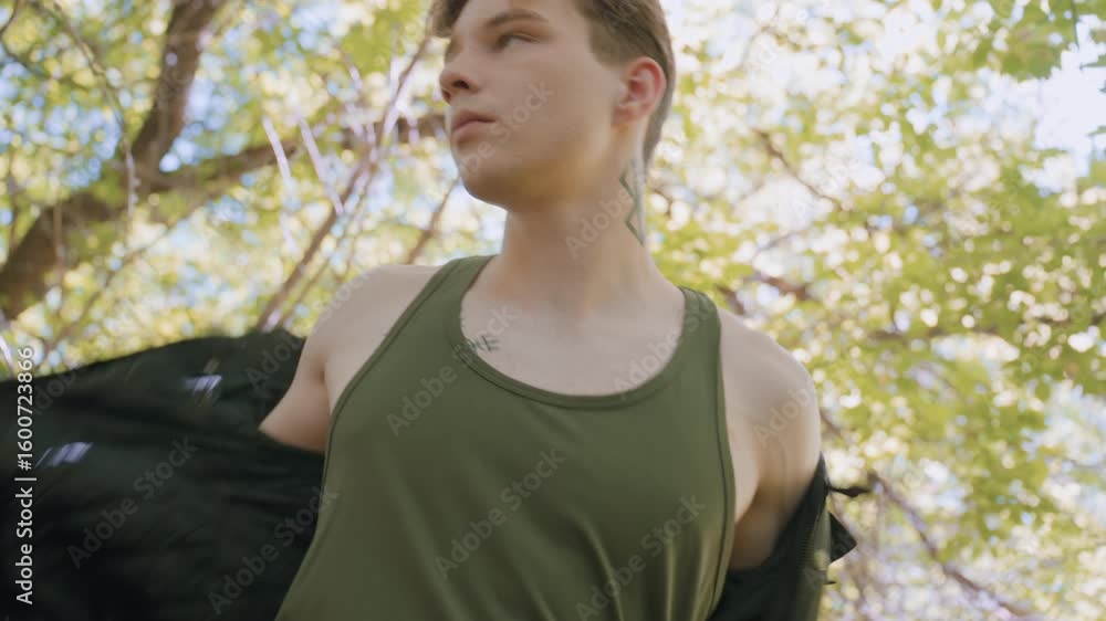 Soldier stands up and looks in different directions while putting on jacket, trying to listen attentively for any strange movements in the surrounding forest environment, preparing for action Soldier stands up and looks in different directions while putting on jacket, trying to listen attentively for any strange movements in the surrounding forest environment, preparing for action