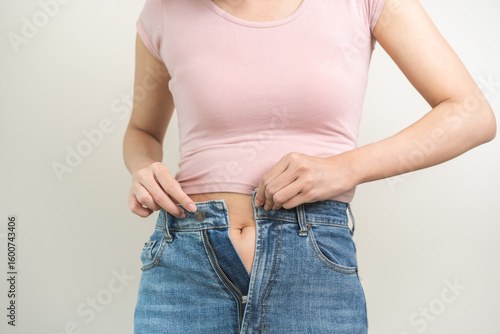 Fotografie Fat belly, chubby asian young woman trying to button tight jeans, obese girl excess fat around waist due to weight gain and a belly