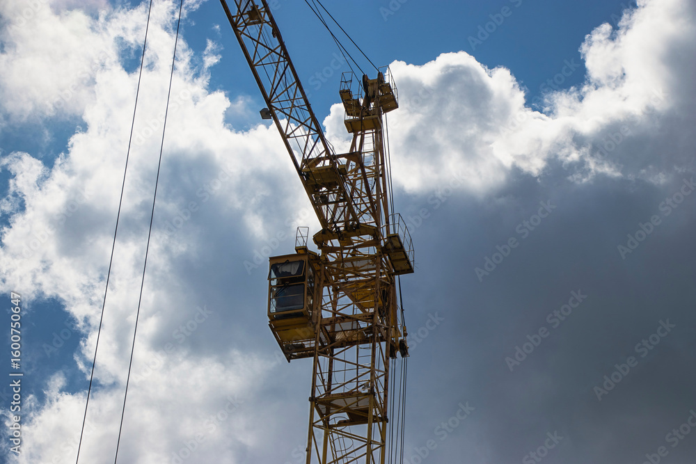 Construction crane towering against a backdrop of dramatic clouds at midday Construction crane towering against a backdrop of dramatic clouds at midday