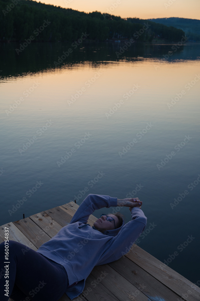 Fototapeta premium Woman lying down on the pier at lake, closeup portrait, summer sunset