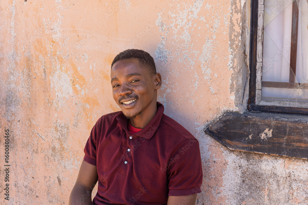 Fototapeta premium Africa village, single smiling young african men resting in front of the house, window and wall