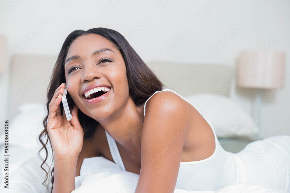 African American woman talking on smartphone while lying on bed in bedroom with pillows and lamp African American woman talking on smartphone while lying on bed in bedroom with pillows and lamp